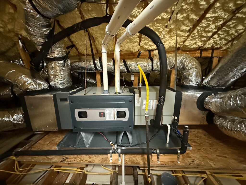 A Trane air handler on a platform in an attic, seen from the side with its drain and gas connections.