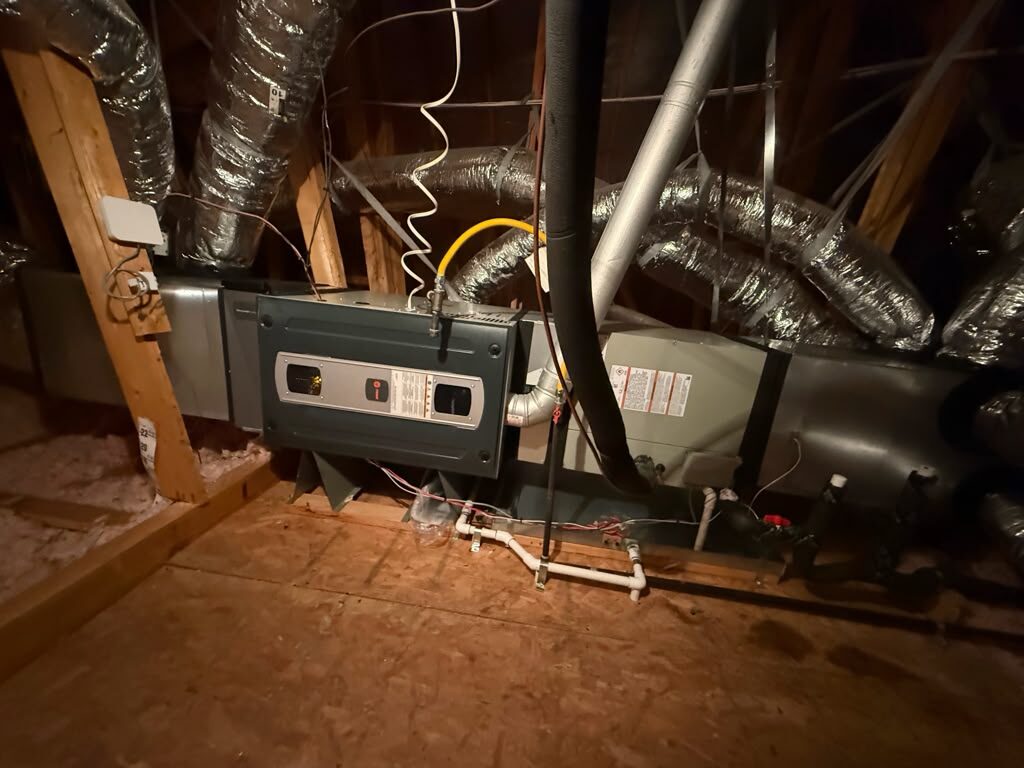 A Trane air handler installed in an attic with a yellow gas line and insulated supply ducts.