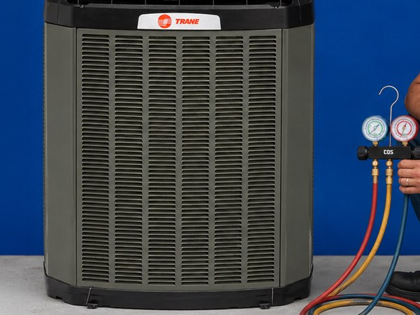 A Trane outdoor condensing unit with a technician holding a manifold gauge set beside it.