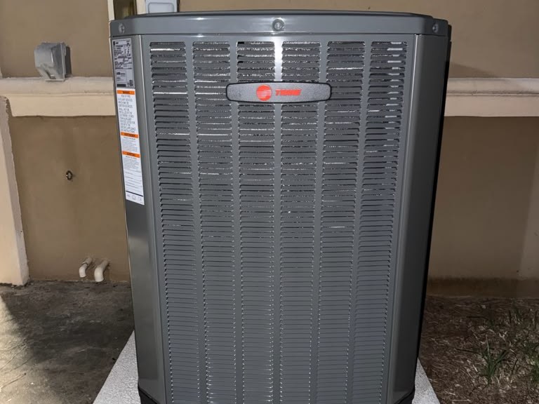 A newly installed Trane outdoor condensing unit on its concrete pad beside a house wall.