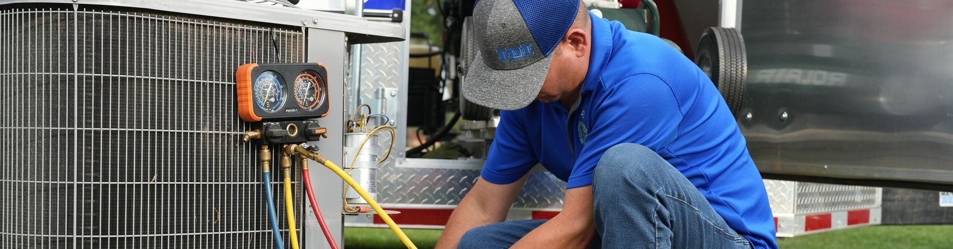 A technician connecting gauge hoses to an outdoor condensing unit beside the RF service trailer.