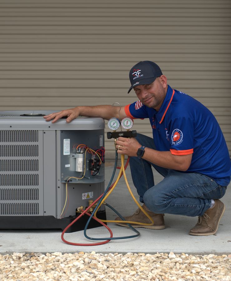 An RF technician kneeling beside a condensing unit and reading a manifold gauge set.