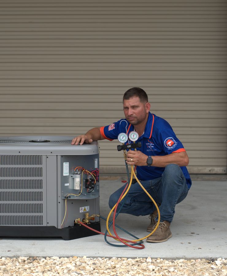 An RF technician kneeling beside a condensing unit with gauge hoses connected.