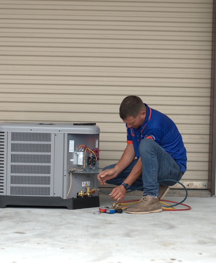 A technician working at the base of an outdoor condensing unit with gauge hoses attached.