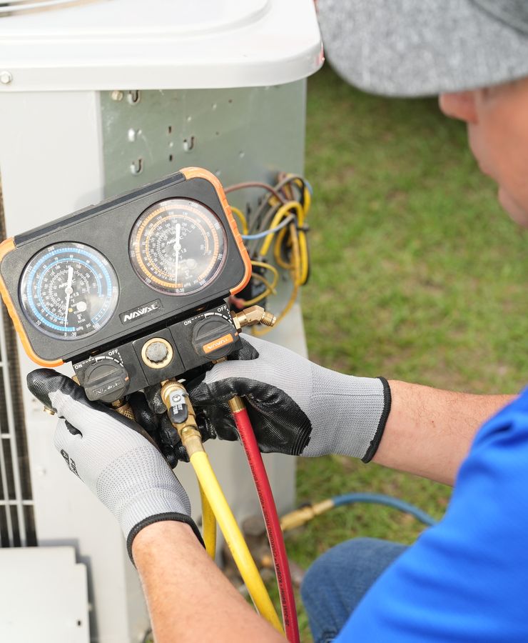 Close view of gloved hands holding a manifold gauge set at a condensing unit.