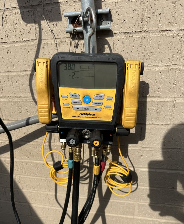 A digital manifold gauge hanging on a wall with its hoses connected.