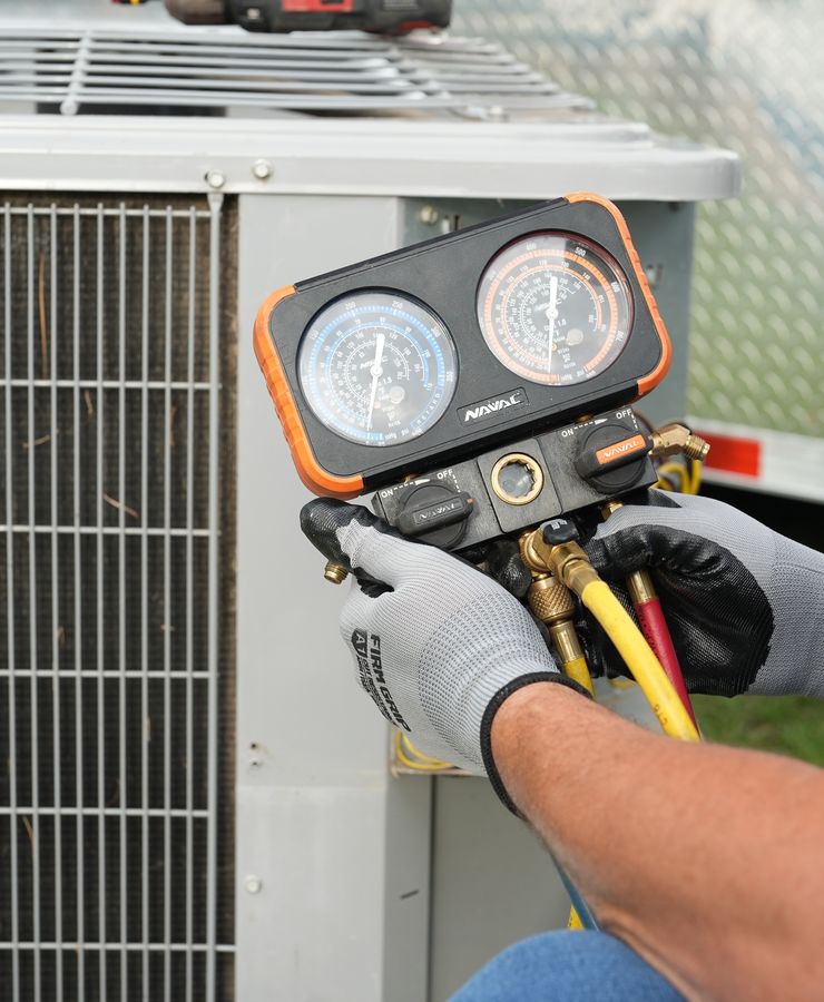 Gloved hands connecting a manifold gauge set to an outdoor condensing unit.