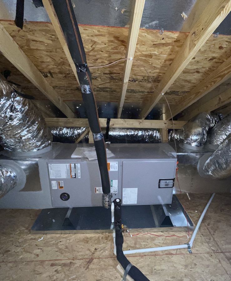 An indoor unit on its platform in an attic, with refrigerant lines and flex ducts.