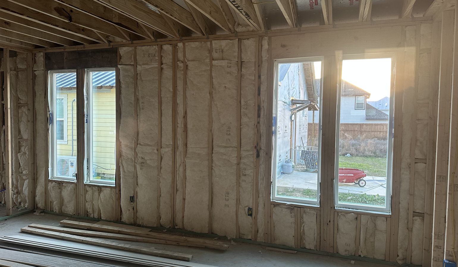 The framed walls of a room covered in fresh spray foam insulation, with the windows in place.