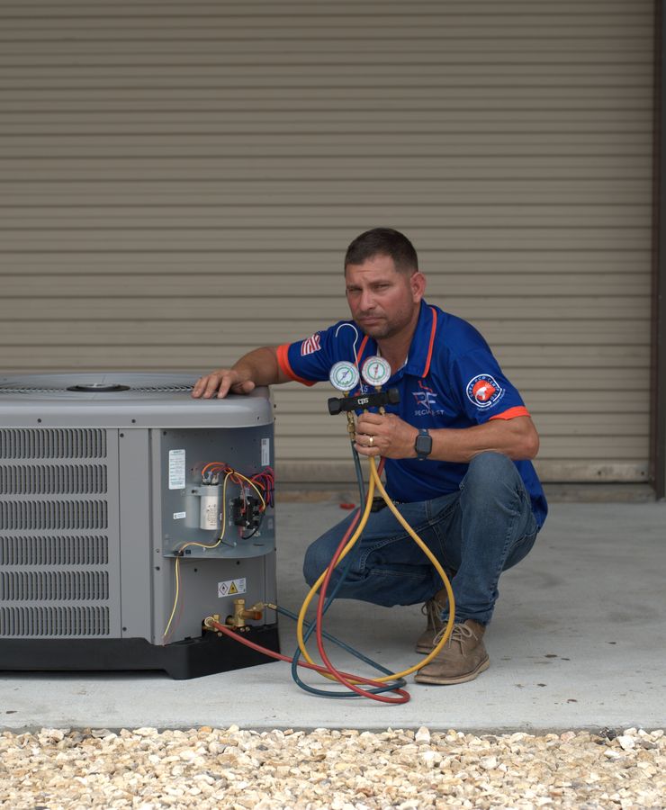 An RF technician reading gauges at a condensing unit during a service visit.