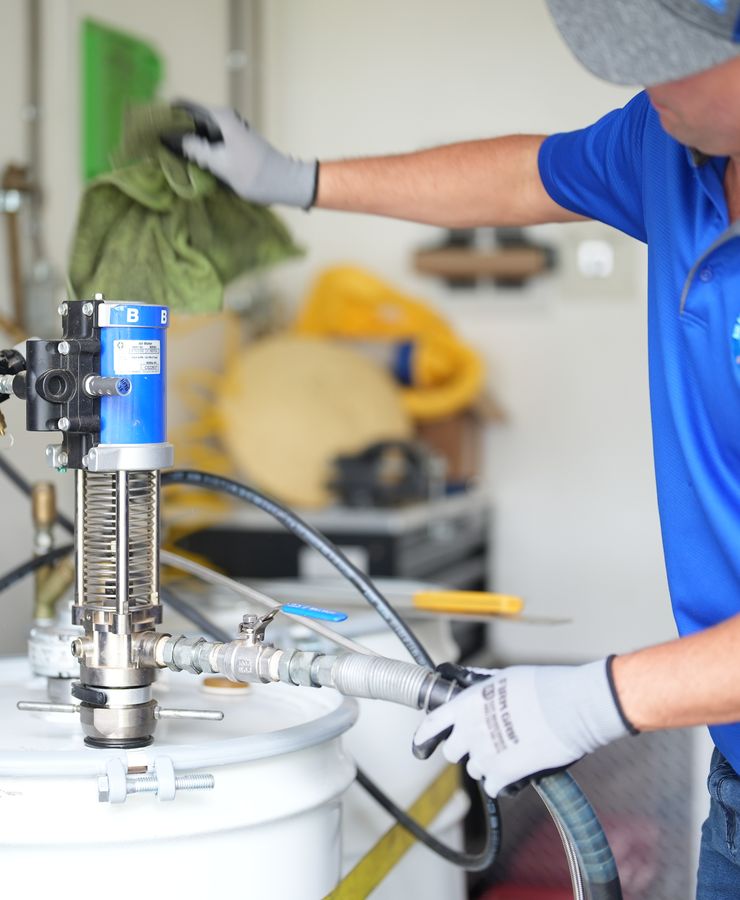 A technician wiping down the spray foam pump at a material drum.